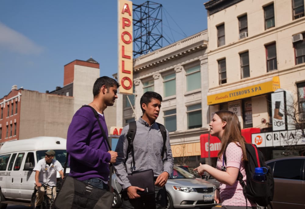 Three students chatting on the street in front of the Apollo Theater in Harlem, NYC.